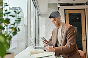 Young busy Asian business man using mobile phone working in office.