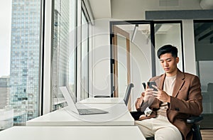 Young busy Asian business man working using mobile and laptop in office.