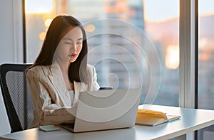 Young busy Asian business woman working using phone and laptop in office.