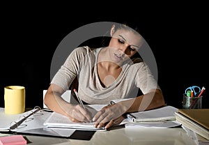 Young busy beautiful Spanish girl studying at home late night looking preparing exam writing on notepad