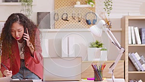 Young busy business woman has curly hair working on project paperwork talking on the phone. woman making business call on mobile