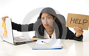 Young busy desperate Latin businesswoman holding help sign sitting at office desk in stress worried