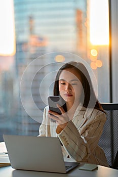 Young busy serious Asian business woman using phone in corporate office.