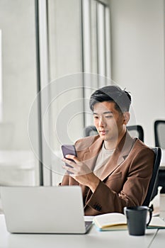 Young busy smiling Asian business man using mobile phone in office.