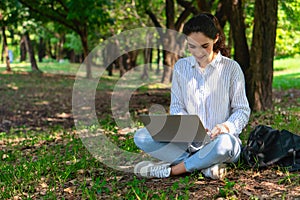 Young caacasian businesswoman sitting under tree in natural park using laptop computer for work outside office