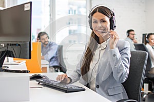 Young call center operator woman in headset working on computer and looking at camera.