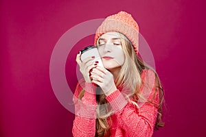 Young Calm Cheerful Caucasian Girl Laughing In Knitted Autumn Hat and Sweater With Cup of Coffee on Red