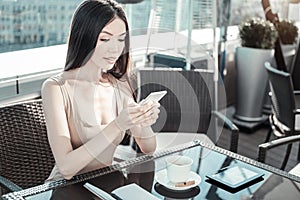 Young calm girl holding cellphone and looking at the screen.