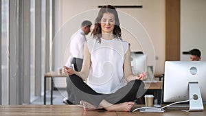 Young calm mindful business woman worker meditate sit on desk