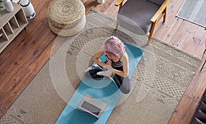 Young calm woman pink hair meditating watching online class at home, top view.