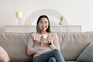 Young calm woman relax, sit on comfortable sofa in modern living room