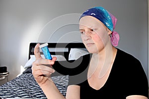 Young cancer patient in a headscarf looks at pill bottle in concern