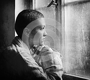 Young cancer patient looking through hospital window in black an
