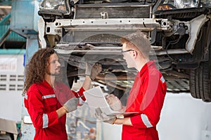 Young car mechanics team in uniform are working in auto service with lifted vehicles. Car repair and maintenance concepts