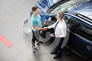 Young car salesman shaking hands with client