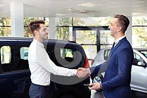 Young car salesman shaking hands with client