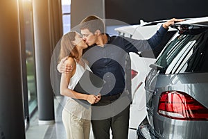 Young car salesman telling about features of car to female customer