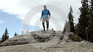 Young, carefree boy climbing up solid huge rocks, using poles to make it easy to reach the top, enjoying the view of