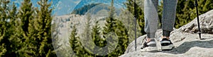 Young, carefree boy climbing up solid huge rocks, using poles to make it easy to reach the top, enjoying the view of natural