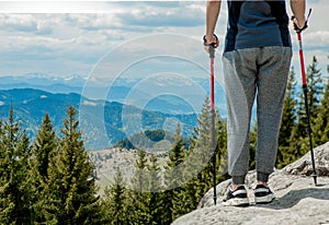 Young, carefree boy climbing up solid huge rocks, using poles to make it easy to reach the top, enjoying the view of natural