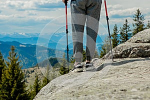 Young, carefree boy climbing up solid huge rocks, using poles to make it easy to reach the top, enjoying the view of natural