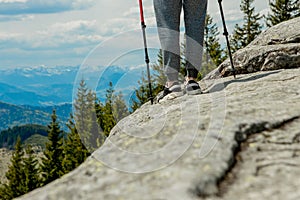 Young, carefree boy climbing up solid huge rocks, using poles to make it easy to reach the top, enjoying the view of natural