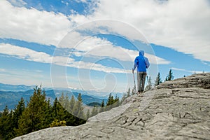 Young, carefree boy climbing up solid huge rocks, using poles to make it easy to reach the top, enjoying the view of natural