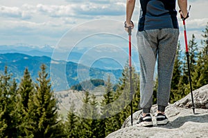 Young, carefree boy climbing up solid huge rocks, using poles to make it easy to reach the top, enjoying the view of natural