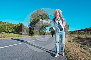 Young carefree woman with backpack travelling by car. Road trip adventure. Woman stopping car with thumbs up