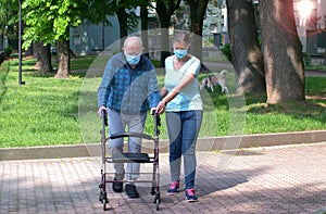 Young caregiver accompanies an elderly gentleman helping him to walk in the park