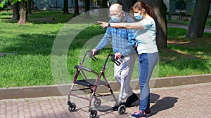 Young caregiver accompanies an elderly gentleman helping him to walk in the park