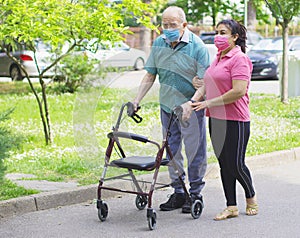 A young caregiver accompanies an elderly gentleman helping him to walk in the park