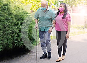 A young caregiver accompanies an elderly gentleman helping him to walk in the park