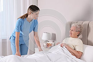 Young caregiver assisting senior woman in bedroom. Home health care service