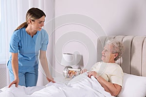 Young caregiver assisting senior woman in bedroom. Home health care service