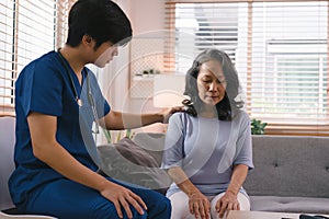 A young caregiver is consulting with a 60-year-old Asian elderly woman, providing encouragement and taking a medical