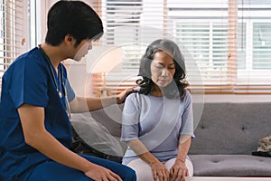 A young caregiver is consulting with a 60-year-old Asian elderly woman, providing encouragement and taking a medical