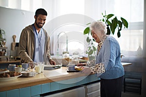 Young caregiver serving breakfast to elderly woman in nursing home care center.