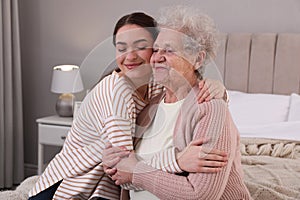 Young caregiver talking to senior woman in bedroom. Home health care service