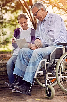 Young carer granddaughter reading book in the park disabled gran