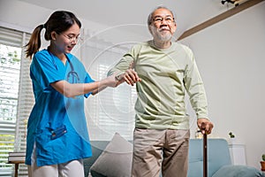 Young carer supporting helping senior man stand up with walking stick from sofa