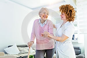 Young carer supporting senior disabled woman with walking stick. Portrait of happy female caregiver and senior woman walking