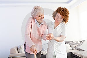 Young carer supporting senior disabled woman with walking stick. Portrait of happy female caregiver and senior woman walking