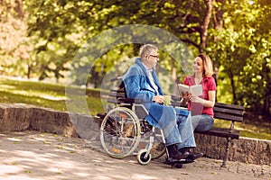 Young carer woman reading book outdoor disabled man in wheelchair.