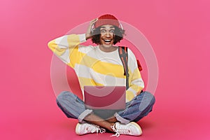 Young caribbean man in headphones laughing and using laptop