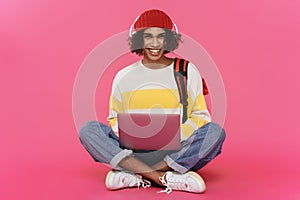 Young caribbean man in headphones smiling and using laptop