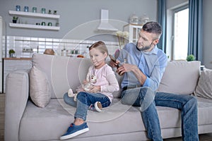 Young caring dad combing hair to little daughter.