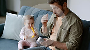 Young caring father measuring body temperature of his playful baby daughter and seeing fever, empty space