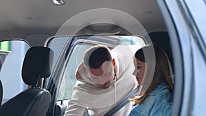 Young caring father opens car door and helps his teenager daughter to get into car and fasten seat belt. Safety drive