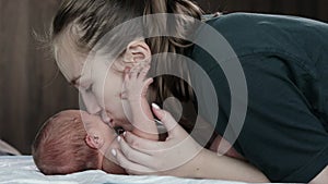 Young caring loving mother kissing her newborn baby boy close up view. Concept of happy motherhood moments, child and